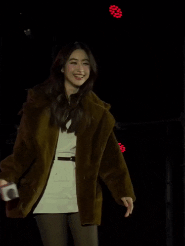 a woman in a brown jacket is holding a microphone in her right hand