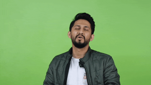 a man with a beard is wearing a green jacket and a white shirt with a sticker on it