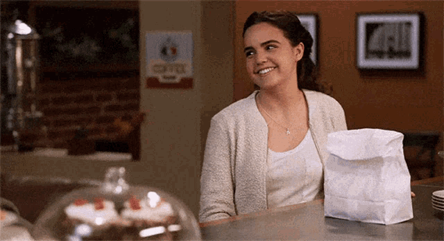 a woman sitting at a counter with a bag of food in front of her and a sign that says coffee