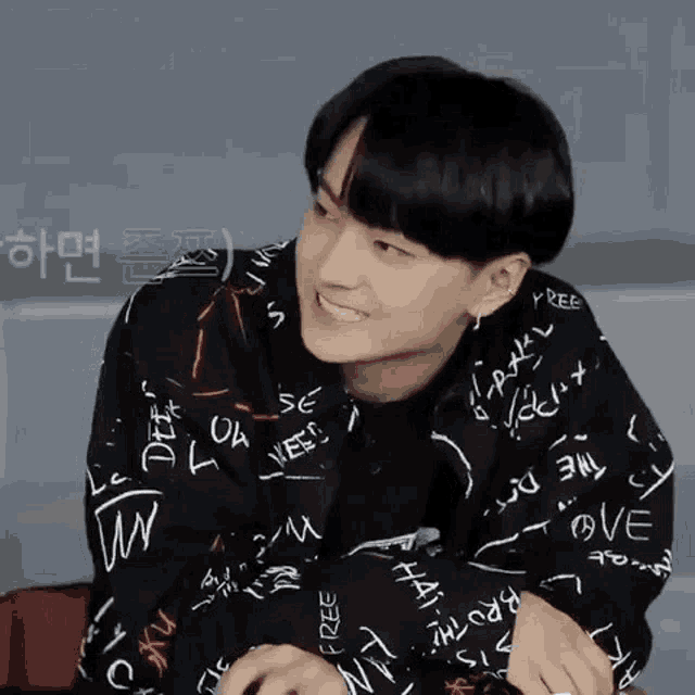 a young man wearing a black jacket with writing on it is smiling and looking at the camera .