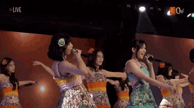a group of girls singing on stage with the word live on the bottom right