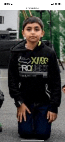 a young boy wearing a black hoodie is kneeling down on the street .