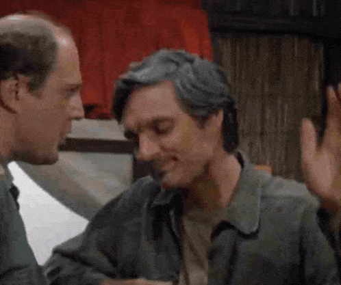two men are talking to each other in a room and one is smiling .