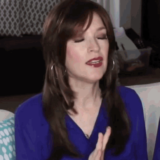 a woman in a blue shirt is sitting on a couch with her eyes closed and her mouth open .