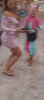 a group of women are dancing on a street and one of them is wearing a pink hijab .