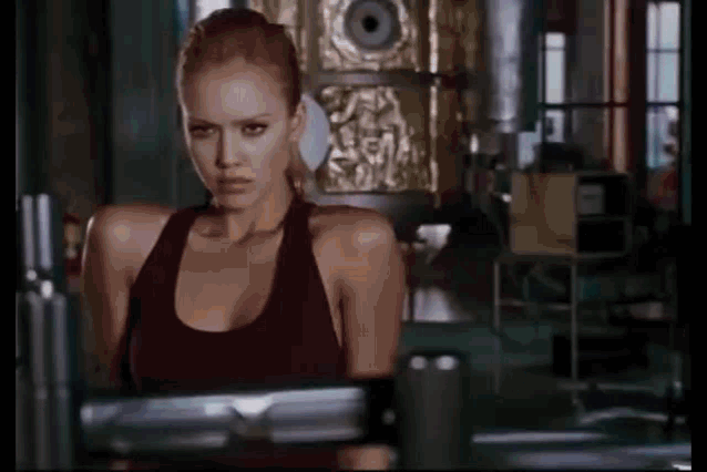 a woman in a red tank top is standing in a gym looking at the camera .