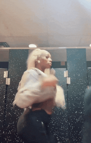 a woman with blonde hair is standing in a bathroom stall