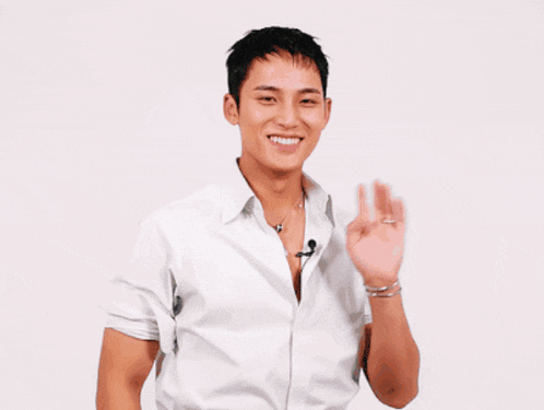 a young man wearing a white shirt is smiling and waving