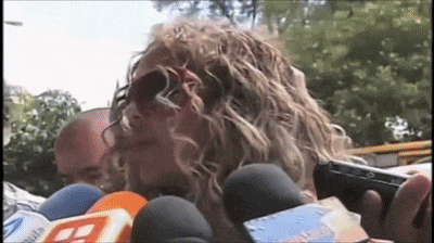 a woman wearing sunglasses is holding a gun and talking into a microphone with a t on it