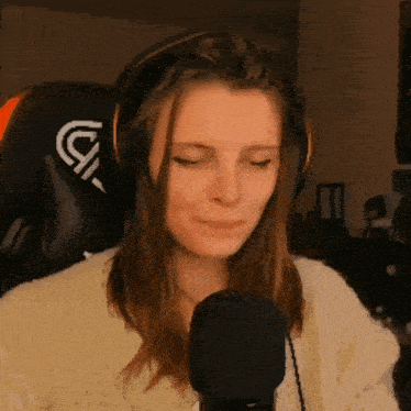 a woman wearing headphones and a white sweater is smiling in front of a microphone