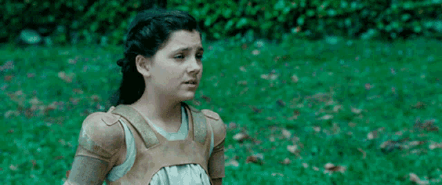 a young girl is standing in the grass wearing a leather vest