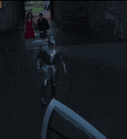 a woman in a red dress is walking behind a man in a knight 's armor