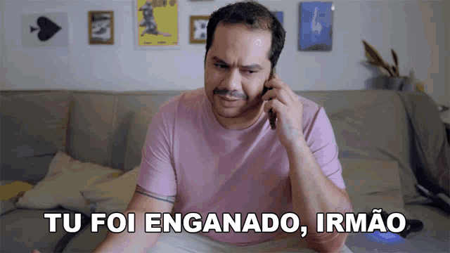 a man sitting on a couch talking on a cell phone with the words tu foi enganado irmao above him
