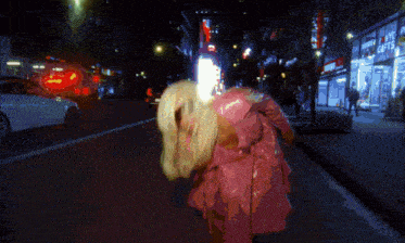 a woman in a pink coat is walking down the street at night