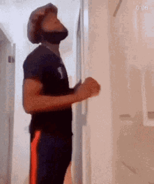 a man wearing a mask and a hat is standing in a hallway looking up .