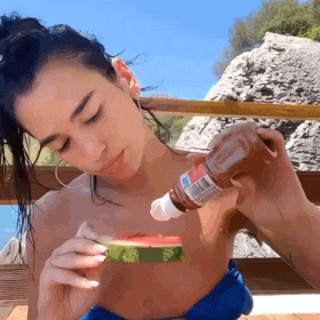 a woman is eating a slice of watermelon while a man pours ketchup on it