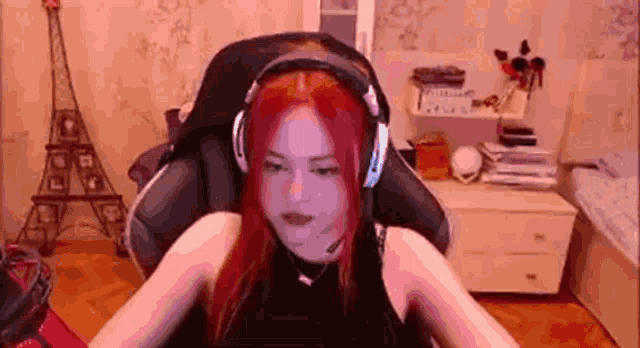 a woman with red hair is wearing headphones and a microphone while sitting in a gaming chair .