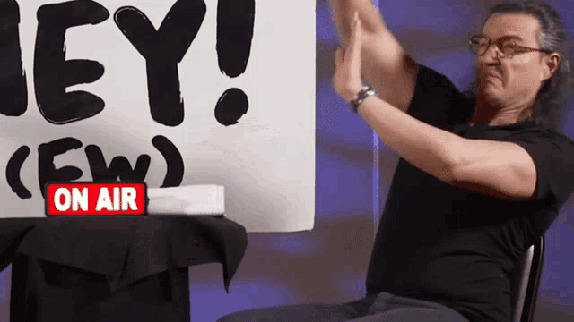 a man is clapping in front of a sign that says " hey "
