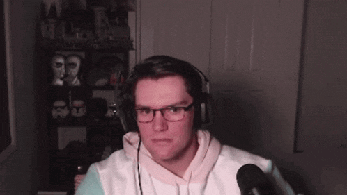 a man wearing headphones and glasses is sitting in front of a microphone in a room .