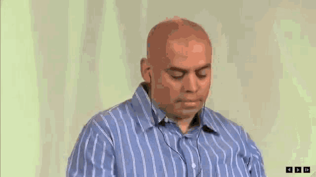 a bald man wearing a blue and white striped shirt and headphones is looking down .