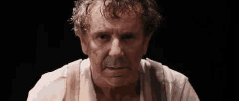 an older man with a beard and a white shirt is looking at the camera .