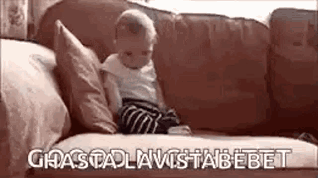 a baby is sitting on a couch with a pillow and a blanket .