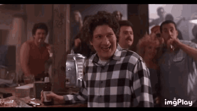 a man in a plaid shirt is holding a bottle of beer in a crowded room .