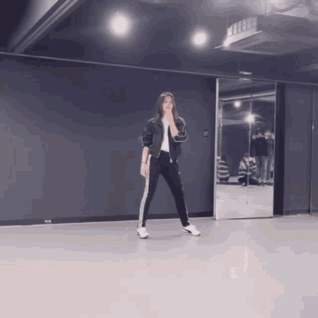 a woman in a black jacket and black pants is standing in front of a mirror