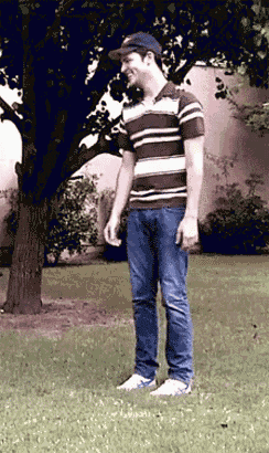 a man wearing a striped shirt and a baseball cap stands in the grass