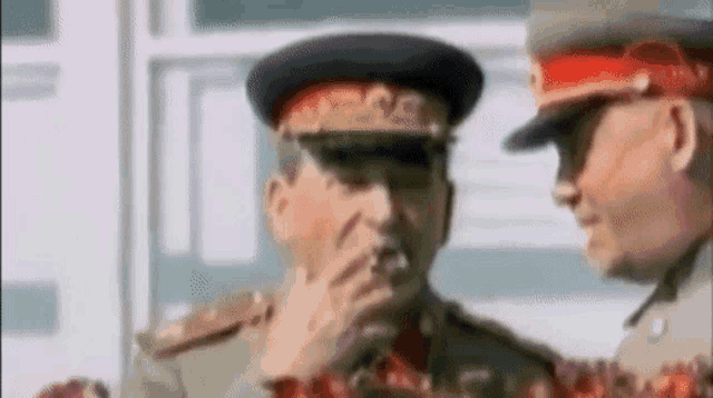 a man in a military uniform is smoking a cigarette next to another man in a military uniform .