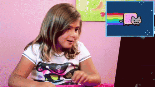a little girl is looking at a laptop with a rainbow cat on the screen