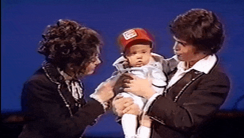 a man and woman are holding a baby in their arms . the baby is wearing a red hat .