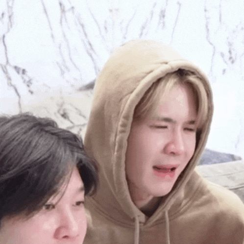 a man in a hoodie is crying while another man looks on .