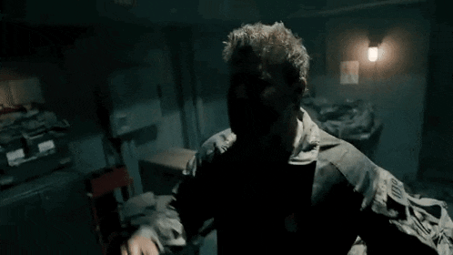 a man in a military uniform is standing in a dark room with his hands up .
