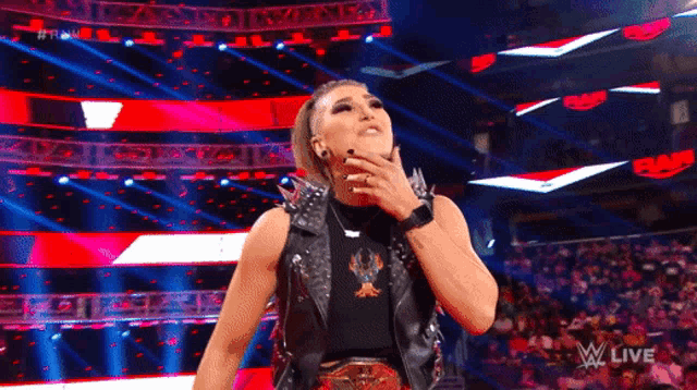 a female wrestler stands in front of a crowd while wearing a black leather vest