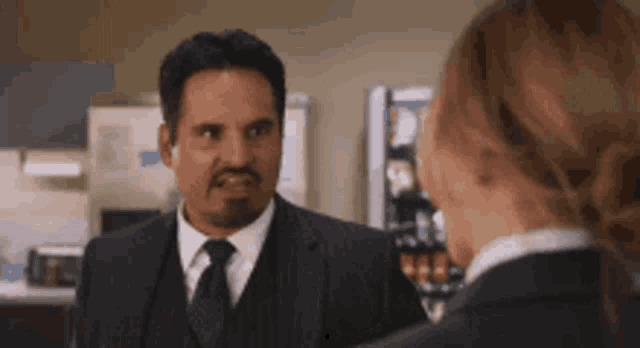 a man in a suit and tie is talking to a woman in a kitchen .