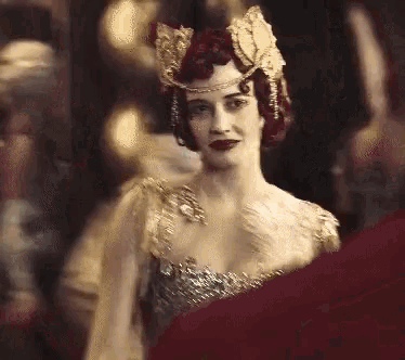 a woman with red hair and a crown on her head is standing in front of a crowd of people .