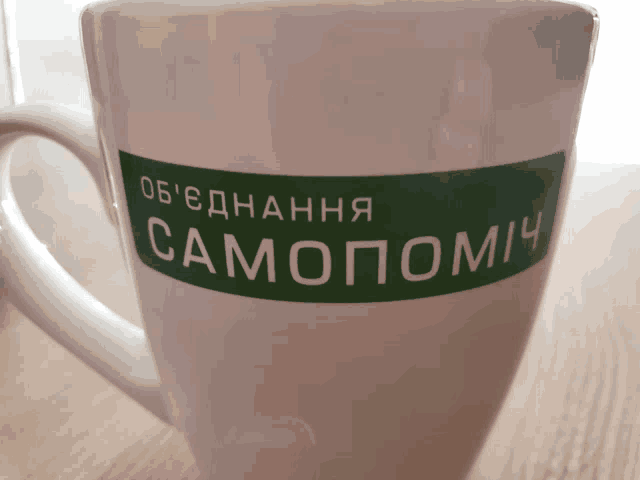 a white coffee mug with a green sticker that says ' samopomi ' on it