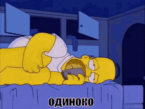 homer simpson is laying on a bed with a phone in his mouth