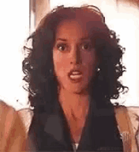 a woman with curly hair is making a surprised face while standing in front of a window .