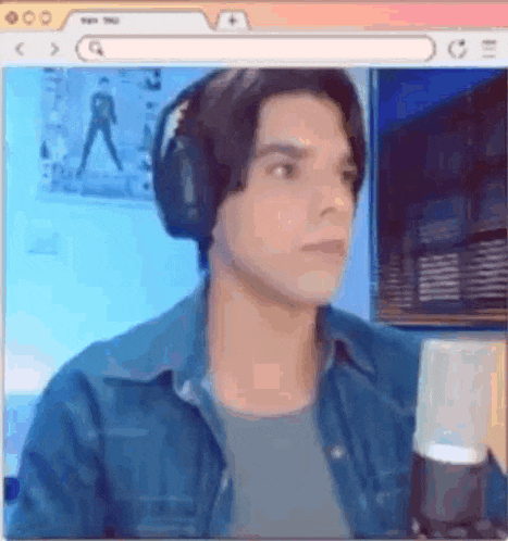a man wearing headphones and a denim shirt is sitting in front of a computer screen .