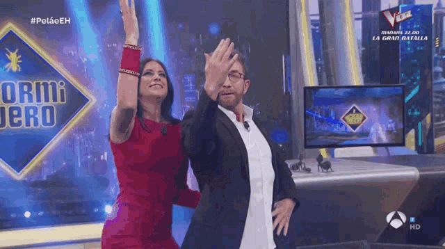 a woman in a red dress stands next to a man in a suit on a stage