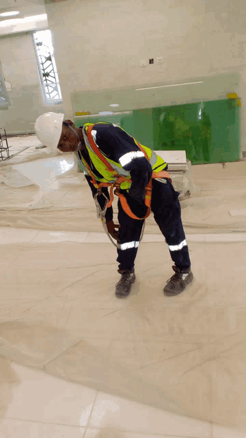 a man wearing a hard hat and safety vest is kneeling down on the floor