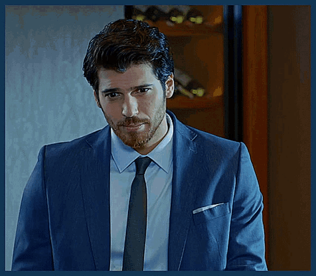 a man with a beard wearing a suit and tie looks at the camera