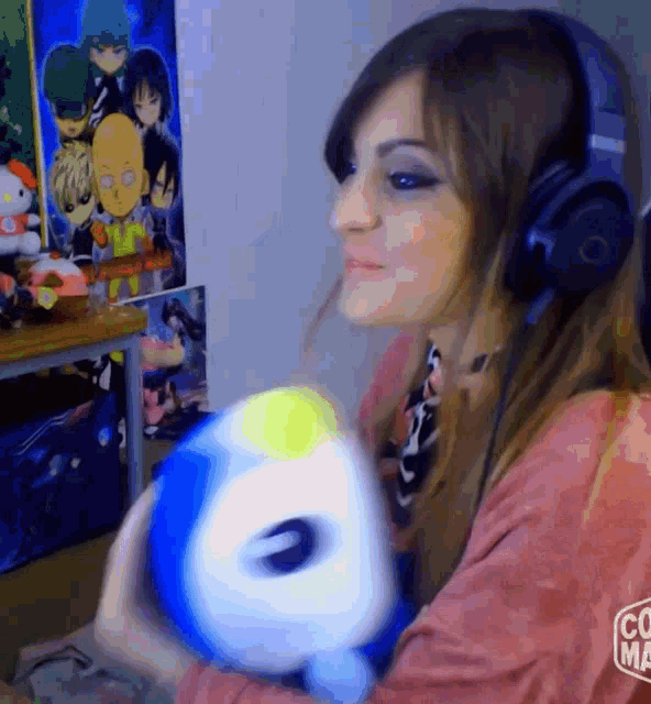 a woman wearing headphones is holding a stuffed animal in front of a wall with anime characters on it