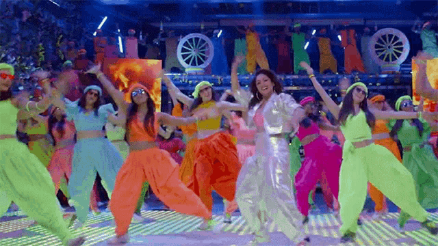 a group of women are dancing on a stage in neon clothes