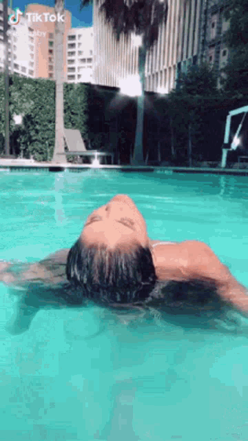 a woman is floating on her back in a swimming pool with her head in the water .
