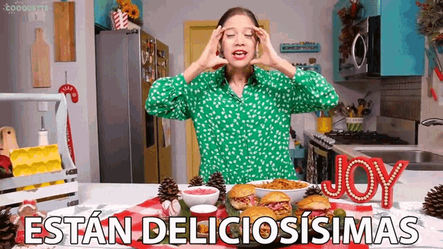 a woman in a green shirt is standing in a kitchen with a sign that says joy in front of her