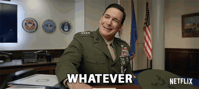 a man in a military uniform is sitting at a desk and smiling with the words whatever behind him