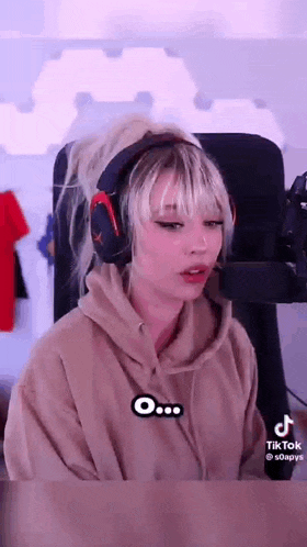 a girl wearing headphones and a hoodie is sitting in front of a microphone .